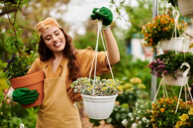 Başörtülü mutlu bir kadın bahçıvan seradaki yemyeşil bitkilerle ilgilenirken gülümsüyor..