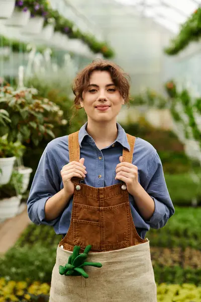 Neşeli genç bir kadın yeşilliklerle çevrili yemyeşil bir serada büyümeye eğilimlidir..