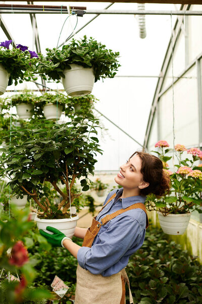 A young woman skillfully tends to thriving plants in a lively greenhouse, surrounded by greenery.