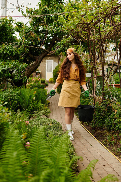 A young woman in an apron and headscarf tends to lush plants while carrying a bucket.