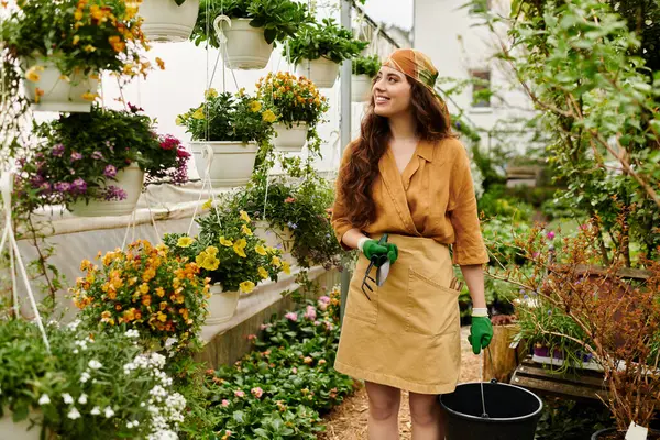 Türbanlı genç bir kadın hayat dolu güneşli bir serada çiçek açma eğilimindedir..