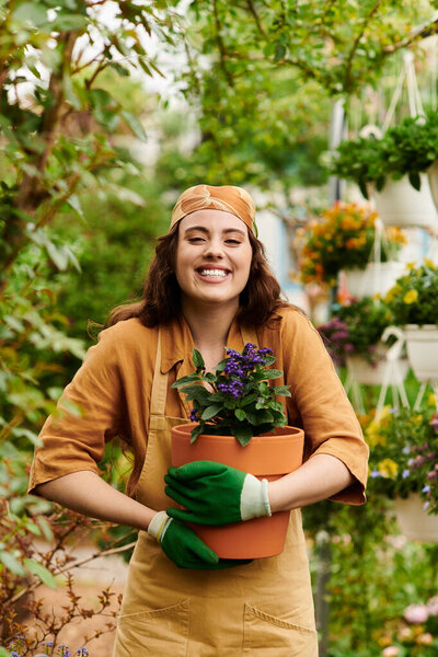 Blissful female gardener in a headscarf smiles while tending to blossoming flowers.