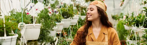 Neşeli genç bir kadın bahçeyle ilgilenirken serada çiçek açan bitkiler, pankartta