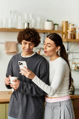 Sıcak bir mutfakta gülümseyen, telefonunu paylaşan ve birlikte eğlenen bir çift..