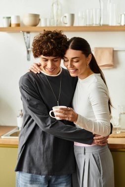 Erkek ve kadın, huzurlu evlerinde kahvelerini yudumlarken birbirlerine sevgiyle sarılıyorlar..
