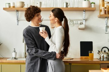 Bir erkek ve bir kadın birbirlerine sevgiyle sarılırken mutfaklarında sıcak bir içki içiyorlar..