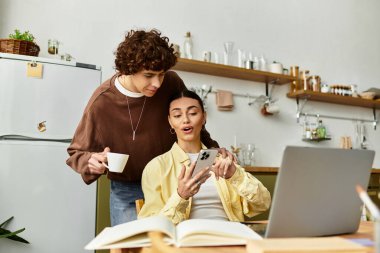 Bir çift mutfak masasına yakın oturuyor, birlikte akıllı telefona bakarken sevinçlerini paylaşıyorlar..
