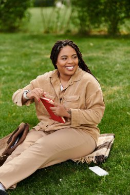 Neşeli bir üniversite öğretmeni çimenlerde oturur, kitap okur ve sıcak güneşin tadını çıkarır..