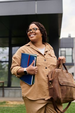Örgülü saçlı bir kadın canlı bir üniversite kampüsünde yürürken ışıl ışıl gülümsüyor..