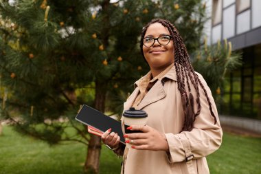 Bir üniversite öğretmeni elinde kahve ve notlar tutarken öğrencilerle yakınlaşarak dışarıda gülümsüyor..