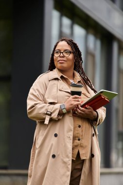 Bir üniversite öğretmeni kahve ve defterlerle dışarıda duruyor, derse hazır..