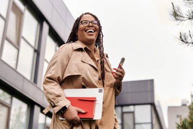 Tabletli ve telefonlu mutlu kadın üniversite binalarının önünde yürürken gülümsüyor..