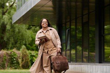 Bir üniversite öğretmeni elinde kitaplarıyla kampüste neşeyle dolaşıyor..