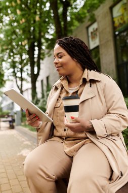 Üniversite öğretmeni rahat rahat oturup tabletini okuyor ve yemyeşil bir ortamda kahvesini yudumluyor..