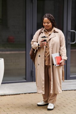 Kadın üniversite binasının önünde durmuş kahvesini yudumluyor ve notlarını gözden geçiriyor..