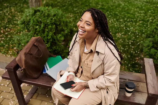 Neşeli bir üniversite öğretmeni açık havada güneşli bir anın tadını çıkarırken fikirlerini defterine kaydeder..