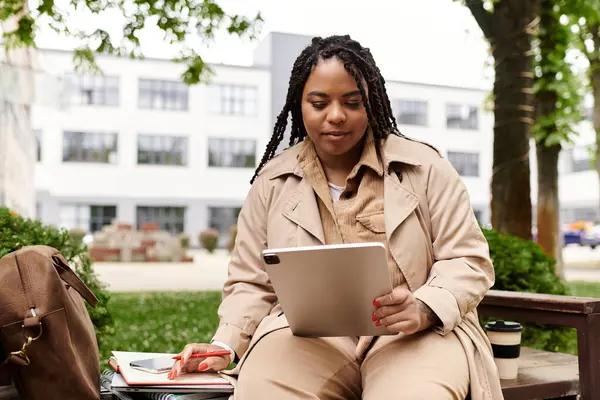 Bir üniversite öğretmeni kampüs bahçesinde otururken tabletteki materyalleri inceler..