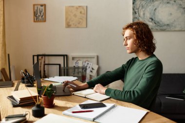 Odaklanmış genç adam, şık çalışma alanında sıcaklıkla dolu yaratıcı işler yapıyor.