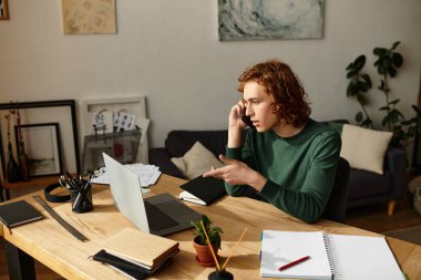 Genç bir adam evdeki masasında oturuyor, telefonda konuşuyor, bitkilerle çevrili iken işine odaklanıyor..