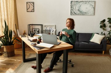 Genç adam modern bir masada oturuyor, sıcak bir içecek yudumluyor, evde yeşillik ve sanatla çevrili..