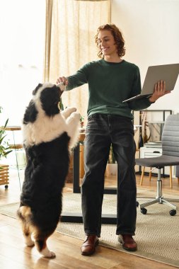Genç bir adam, rahat bir evde iş ve arkadaşlığı dengelemek için köpeğiyle meşgul..