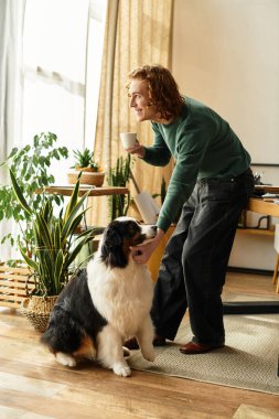 Genç bir adam köpeğiyle birlikte sıcak bir atmosferde kahvesini yudumlarken gülümsüyor..