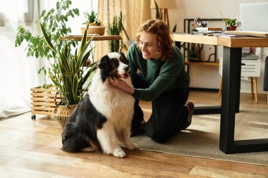 Genç bir adam yeşil ve doğal ışıkla çevrili rahat bir odada köpeğiyle oynuyor..