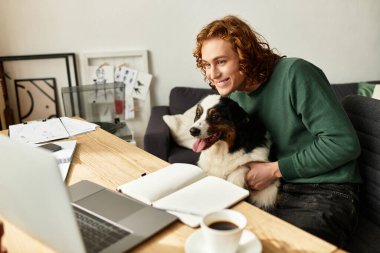 Genç bir adam köpeğiyle evde rahatlar, kahvesini yudumlar ve online aktivitelerden zevk alır..