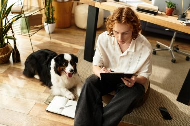 Genç bir adam evinde oturuyor, köpeği yakınlarda dinleniyor, rahat bir ortam yaratıyor..