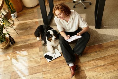 Genç adam, güneşli bir günde sadık köpeği yanında kalırken evde rahatlar ve notlar yazar..