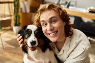 Genç bir adam evinde köpeğiyle eğlenirken gülümser..