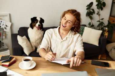 Genç bir adam rahat bir odada ahşap bir masada oturuyor ve köpeğiyle birlikte notlar yazıyor..