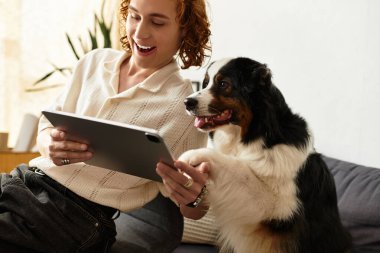 Genç bir adam evde dinleniyor, tablet kullanırken köpeğiyle keyifli bir anı paylaşıyor..