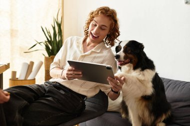 Neşeli köpeği yanında otururken genç bir adam tabletiyle evde dinleniyor..