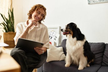 Genç bir adam, köpeğiyle şık bir oturma odasında, tablet kullanarak rahat bir anın tadını çıkarıyor..