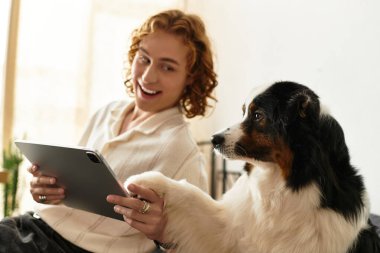 Evde dinlenen genç bir adam, tablet kullanırken köpeğiyle keyifli bir anı paylaşıyor..