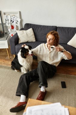 Genç bir adam köpeğiyle yerde dinleniyor, sıcak bir fincan kahvenin tadını çıkarıyor..