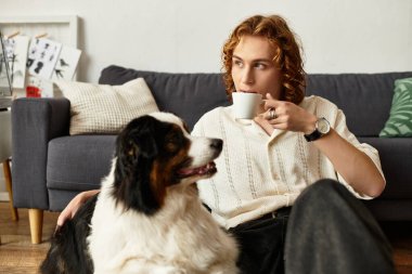 Genç adam köpeğiyle birlikte yerde dinleniyor, rahat bir evde kahvesini yudumluyor..