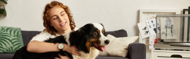 Genç bir adam evinde rahatlar, koltukta otururken köpeğiyle neşe içinde iletişim kurar..
