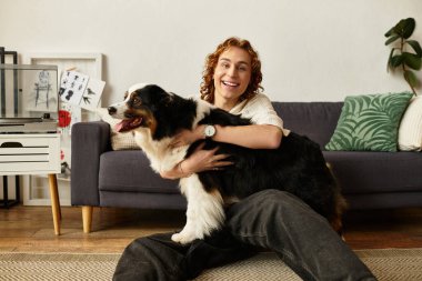 Neşeli genç bir adam evdeki bir kanepede rahatça dinlenirken köpeğini kucaklıyor..