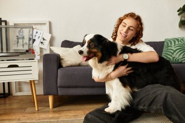 Mutlu bir genç adam evde rahatlar, yerde otururken neşeli köpeğini kucaklar..