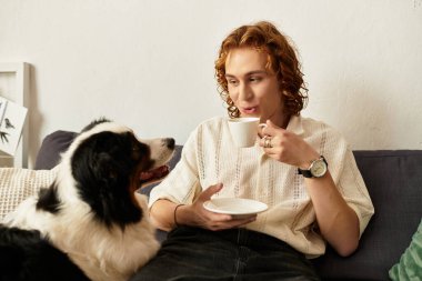 Genç adam sıcak bir anın tadını çıkarıyor, evde köpeğiyle uğraşırken kahvesini yudumluyor..