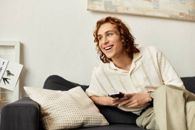 Rahat, kıvırcık saçlı genç adam, oturma odasında televizyon izlerken gülümsüyor..