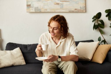 Genç adam evinde sıcak bir içeceğin keyfini çıkarıyor. Etrafı konfor ve sakinlikle çevrili..