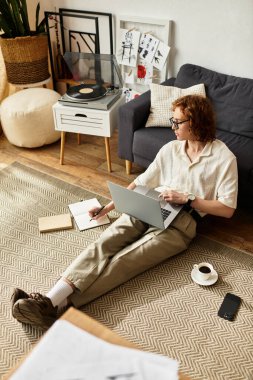 Gündelik kıyafetli genç adam yere oturur, dizüstü bilgisayarına odaklanır ve hafif bir müzik çalar..