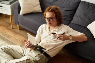 Genç bir adam evde yerde dinleniyor, not defterine yazarken kahvesini yudumluyor..