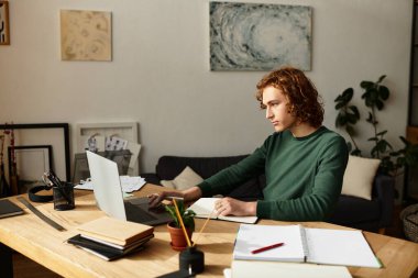 Evde dinlenen genç bir adam, sakin bir dekorla çevrili bir laptopla dikkatle masasında çalışıyor.