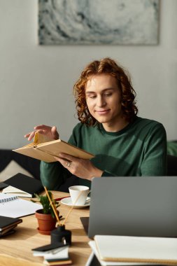 Genç bir adam ahşap bir masada oturuyor, etrafı kitaplarla çevriliyken okuma ve düşünme ile meşgul..