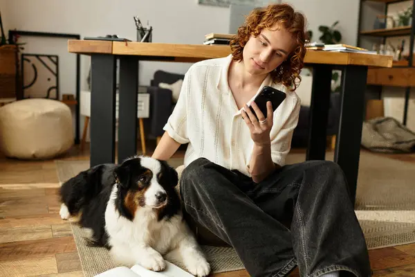 Genç bir adam, köpeği yakınlarda dinlenirken akıllı telefonuyla konuşuyor ve yerde dinleniyor..