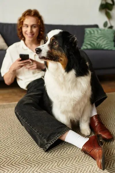 Genç bir adam, hem rahat hem de neşeli görünen köpeğiyle birlikte yerde rahatça oturuyor..